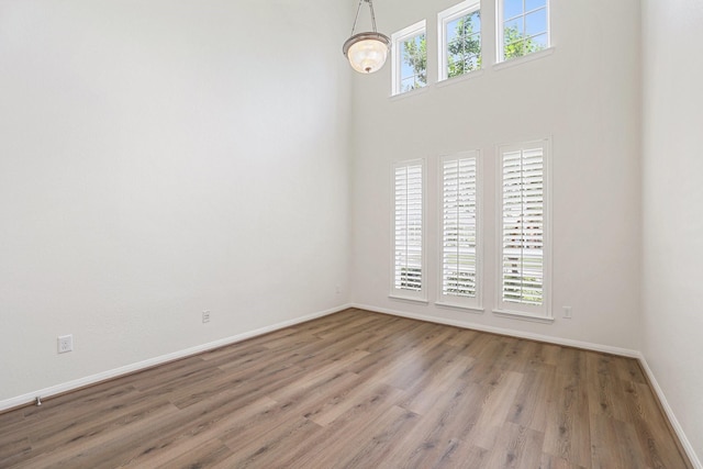 unfurnished room featuring a high ceiling, baseboards, and wood finished floors