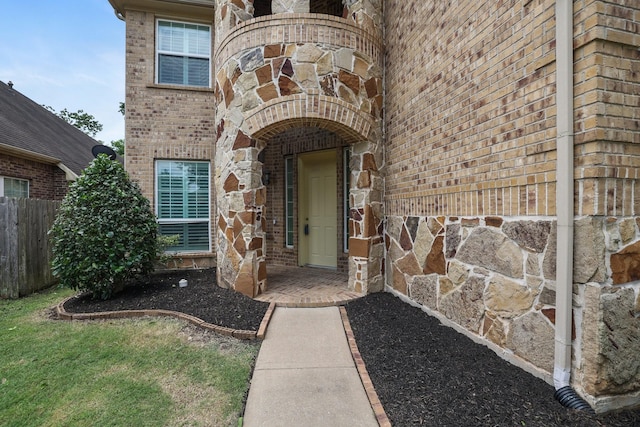 doorway to property with stone siding, brick siding, and fence