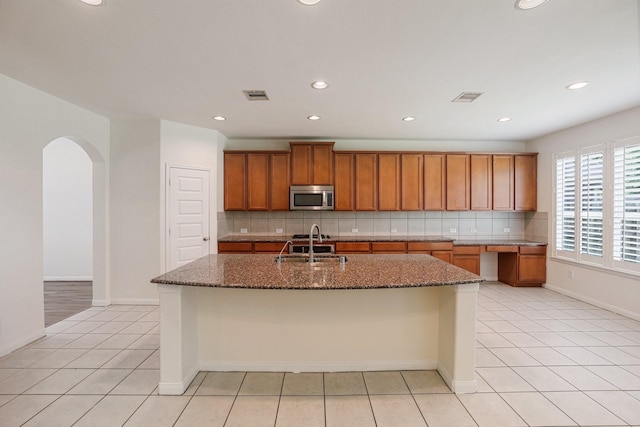 kitchen with brown cabinets, stainless steel microwave, a sink, and visible vents