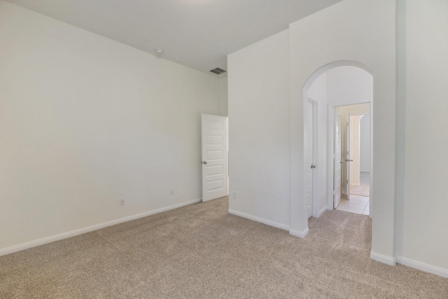 unfurnished room featuring arched walkways, light colored carpet, visible vents, and baseboards