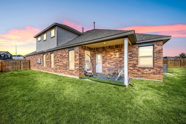 rear view of property featuring a shingled roof, fence private yard, brick siding, and a lawn