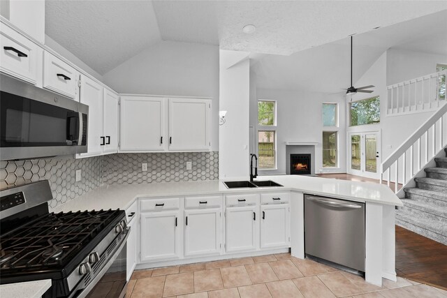 kitchen with light countertops, appliances with stainless steel finishes, open floor plan, a sink, and a peninsula