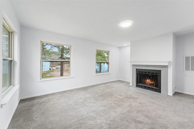 unfurnished living room featuring visible vents, baseboards, a tile fireplace, carpet, and a textured ceiling