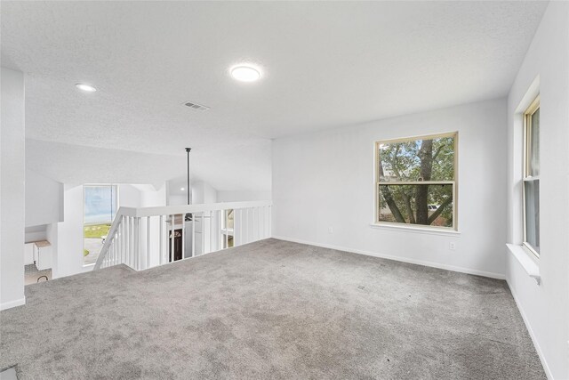 carpeted empty room with visible vents, vaulted ceiling, a textured ceiling, and baseboards