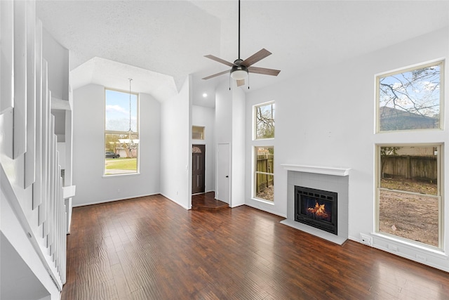 unfurnished living room featuring high vaulted ceiling, wood-type flooring, a tiled fireplace, and ceiling fan with notable chandelier