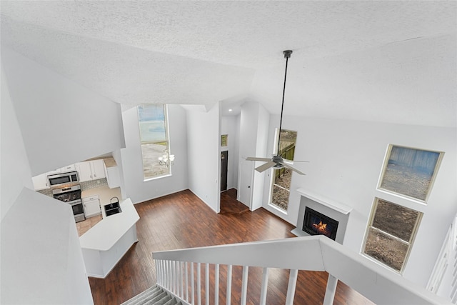 living room with vaulted ceiling, a textured ceiling, wood finished floors, a lit fireplace, and ceiling fan with notable chandelier