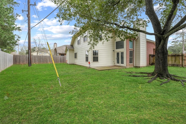 rear view of house with french doors, a lawn, a chimney, and a fenced backyard