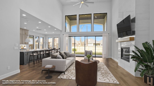 living room with a tile fireplace, wood finished floors, visible vents, a towering ceiling, and baseboards