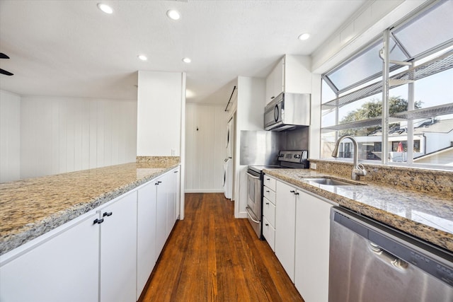 kitchen with white cabinets, light stone countertops, stainless steel appliances, and a sink