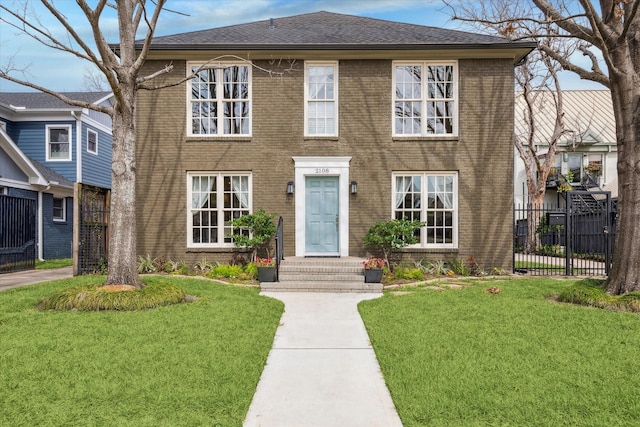 colonial house with roof with shingles, a front yard, fence, and brick siding