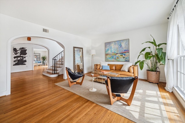 living area with baseboards, visible vents, arched walkways, stairs, and light wood-style floors