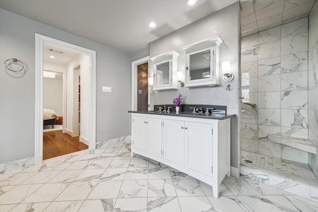 bathroom with marble finish floor, a tile shower, a sink, and double vanity