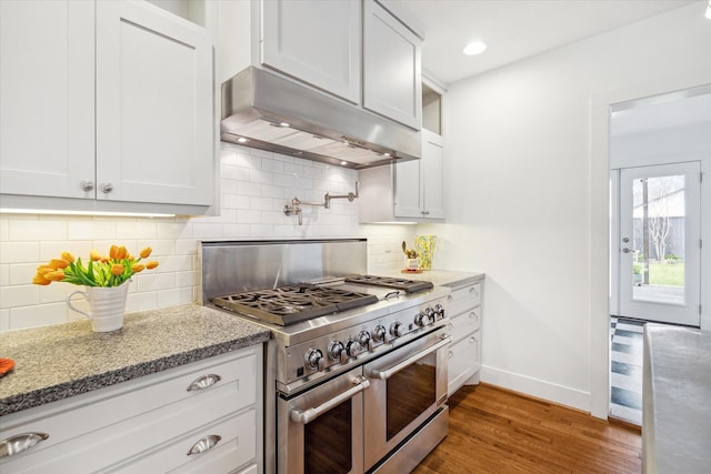 kitchen featuring range with two ovens, light stone counters, wood finished floors, under cabinet range hood, and baseboards