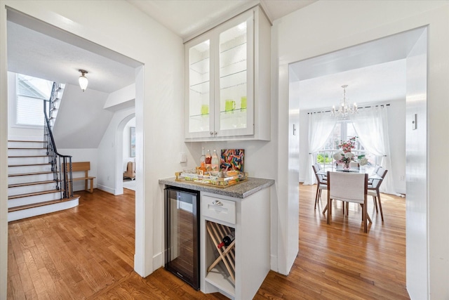 bar featuring wine cooler, stairs, light wood-type flooring, a bar, and plenty of natural light