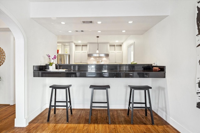 kitchen with under cabinet range hood, a peninsula, wood finished floors, visible vents, and freestanding refrigerator