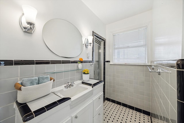 bathroom featuring a tile shower, wainscoting, vanity, and tile walls