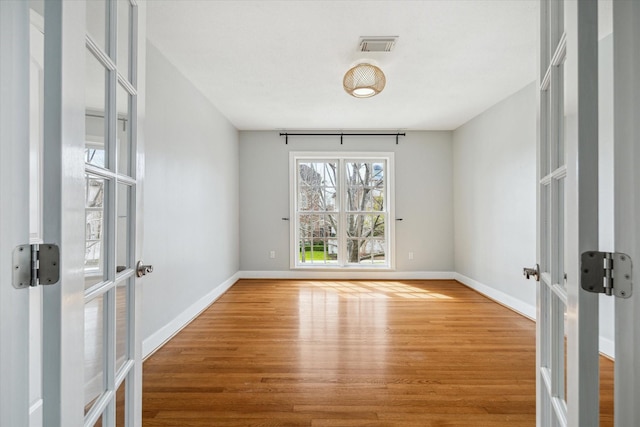 unfurnished room with baseboards, visible vents, wood finished floors, and french doors