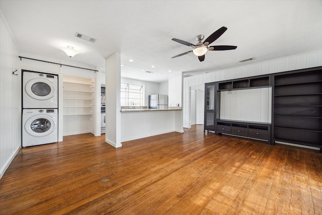 unfurnished living room with stacked washer and dryer, wood-type flooring, visible vents, and a ceiling fan