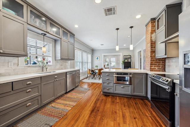 kitchen with visible vents, a peninsula, stainless steel appliances, gray cabinetry, and a sink