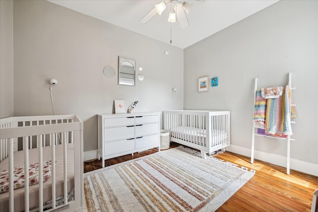 bedroom featuring a ceiling fan, a nursery area, baseboards, and wood finished floors