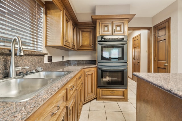 kitchen featuring light tile patterned floors, stainless steel double oven, a sink, and brown cabinetry