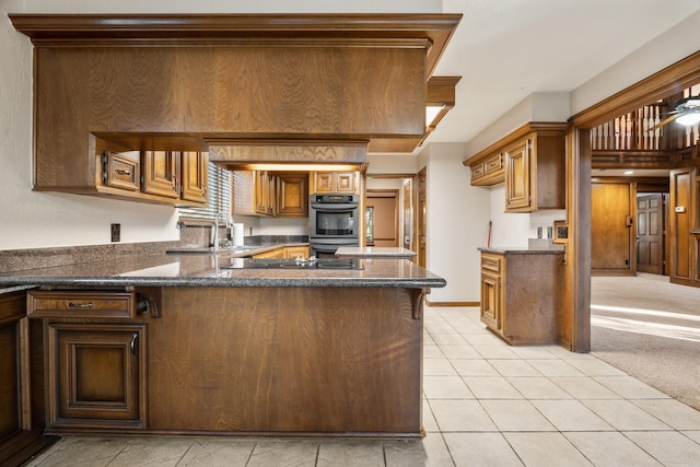 kitchen with brown cabinets, black electric stovetop, light tile patterned floors, double oven, and a peninsula