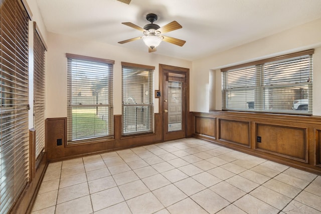 empty room with a ceiling fan, wainscoting, and light tile patterned floors