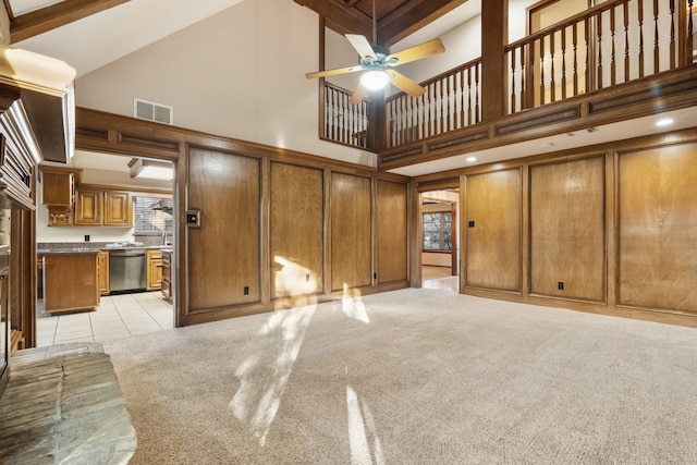 unfurnished living room with light tile patterned floors, visible vents, light colored carpet, a towering ceiling, and ceiling fan