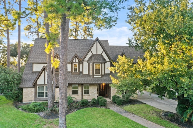 tudor home with stucco siding, a shingled roof, and a front yard