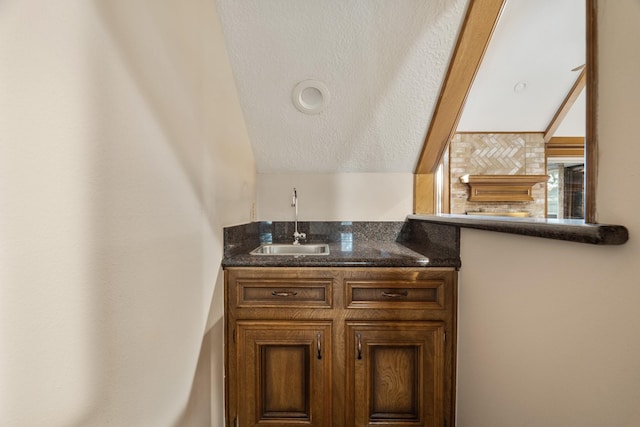 bar featuring a textured ceiling, a sink, and lofted ceiling