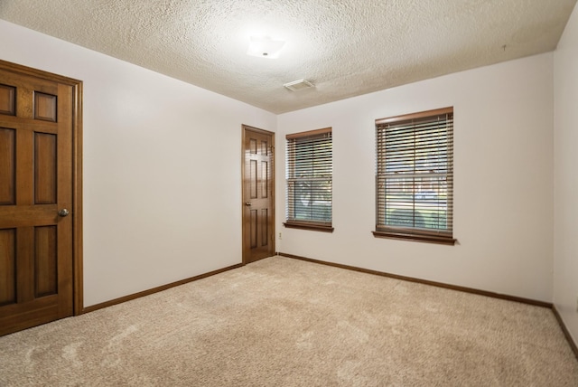 carpeted spare room with a textured ceiling, visible vents, and baseboards