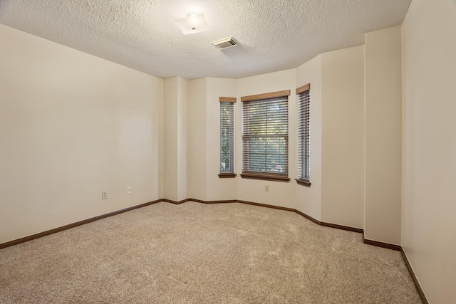 spare room with baseboards, visible vents, a textured ceiling, and light colored carpet