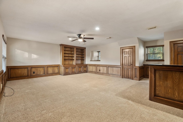 unfurnished living room featuring carpet, a wainscoted wall, and visible vents