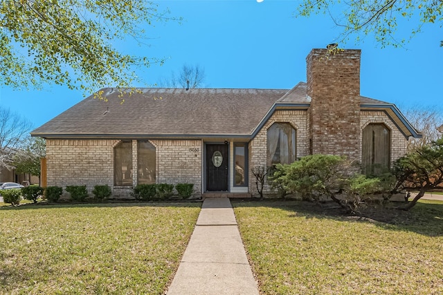 english style home featuring brick siding, a chimney, roof with shingles, and a front yard