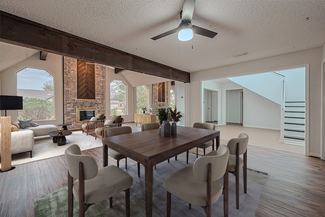 dining space featuring a textured ceiling, a brick fireplace, ceiling fan, and vaulted ceiling with beams