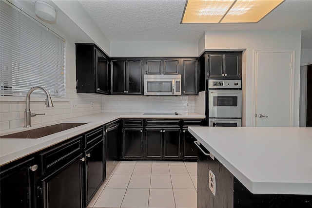 kitchen with a sink, light tile patterned floors, decorative backsplash, stainless steel appliances, and dark cabinets