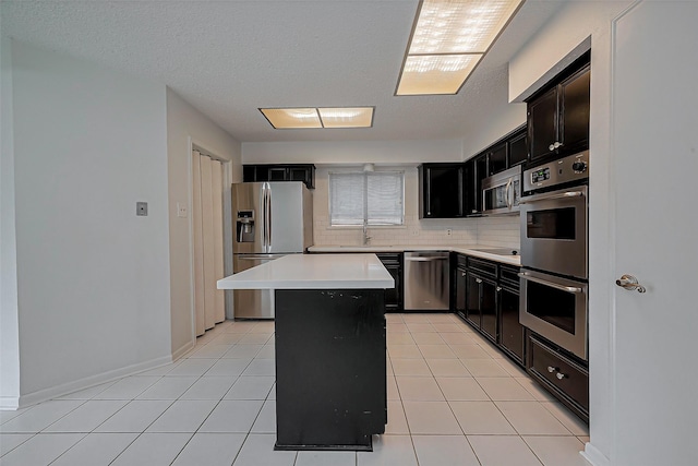 kitchen with dark cabinetry, stainless steel appliances, light countertops, light tile patterned floors, and decorative backsplash