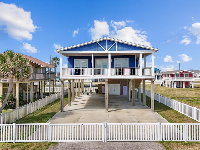 raised beach house with a fenced front yard, a front lawn, a carport, and concrete driveway