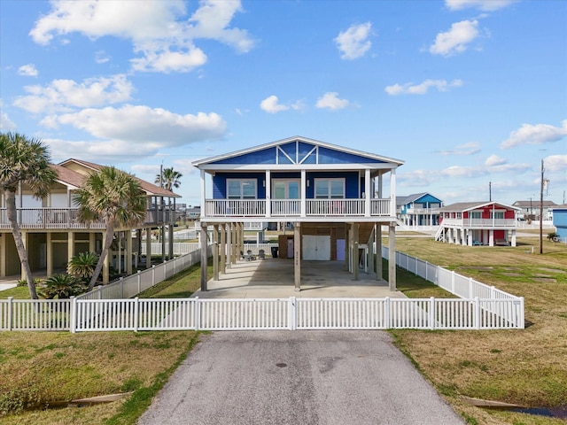 coastal inspired home featuring a fenced front yard, aphalt driveway, and a carport