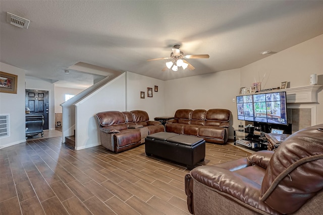 living area with a ceiling fan, wood finish floors, visible vents, and stairs