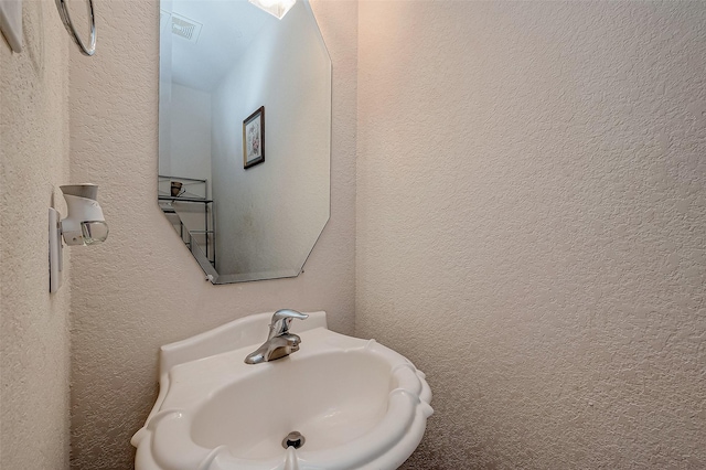 bathroom featuring visible vents, a sink, and a textured wall