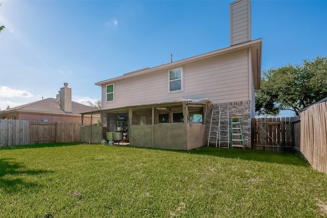 back of property with a chimney, brick siding, a yard, and a fenced backyard