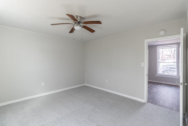 carpeted spare room featuring baseboards and a ceiling fan