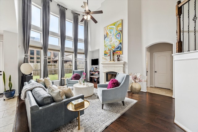 living room with a high ceiling, a fireplace, arched walkways, and wood finished floors