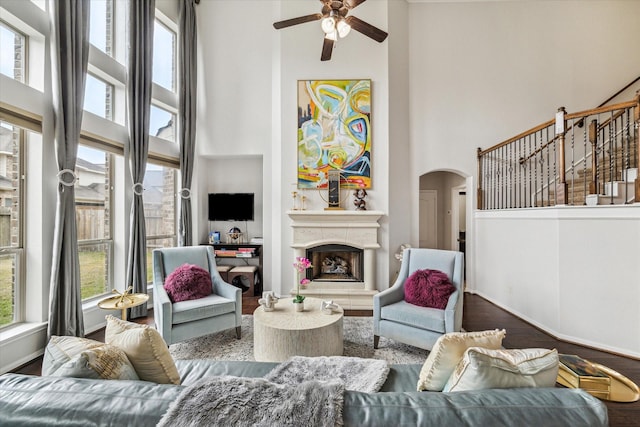 living area featuring arched walkways, a fireplace with raised hearth, wood finished floors, and a towering ceiling