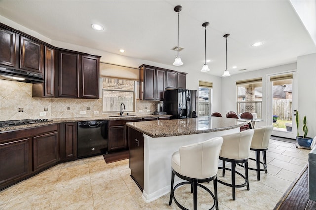 kitchen with a breakfast bar, a sink, a kitchen island, under cabinet range hood, and black appliances