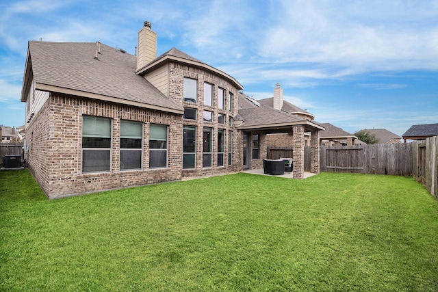 back of property featuring a patio area, brick siding, a chimney, and a lawn