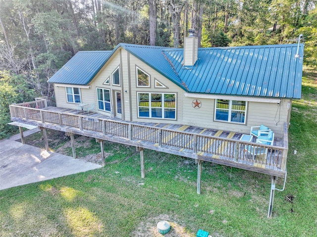 rear view of house with metal roof, a chimney, a wooden deck, and a lawn