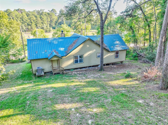 back of property with a chimney, cooling unit, metal roof, and a lawn