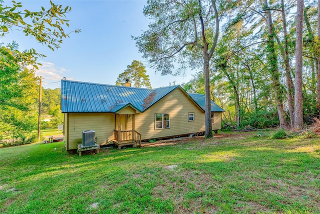 rear view of house featuring cooling unit, metal roof, a chimney, and a lawn